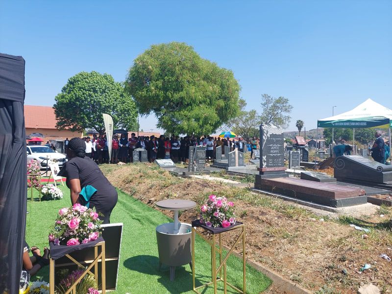 A floral arrangement on a gold stand at a BaAfrica graveside setup