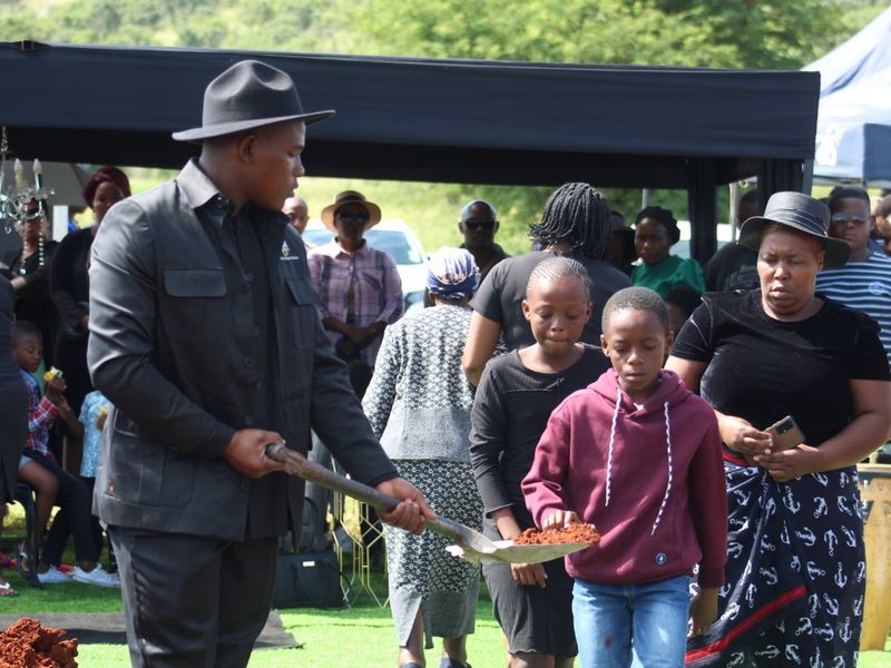 Children taking part in the traditional filling of the grave, assisted by a BaAfrica attendant