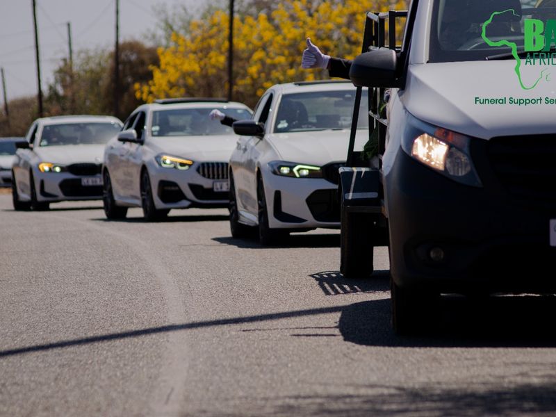 The BaAfrica fleet of white family cars lined up behind the hearse