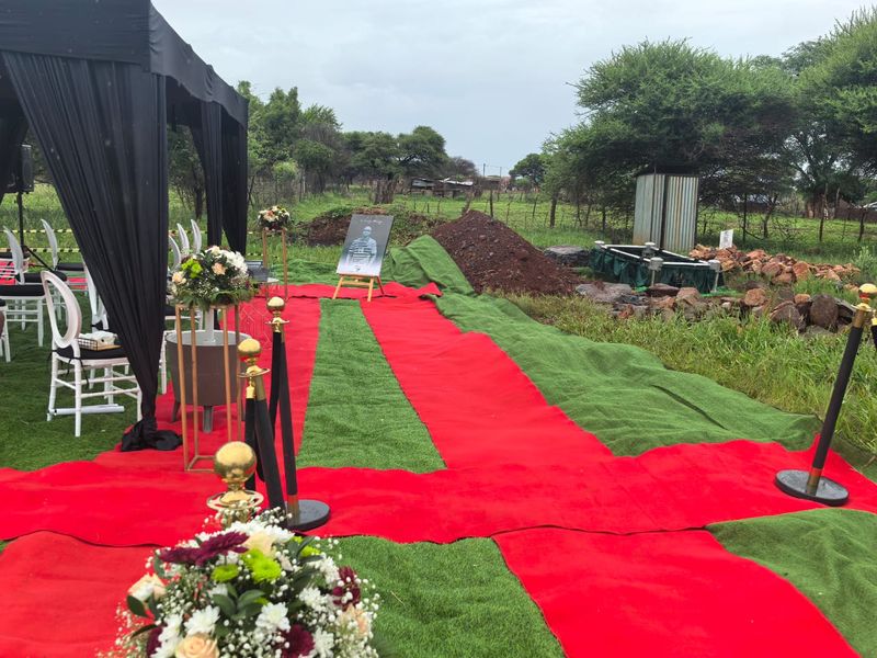 Graveside setup with red carpet laid across green turf and a black draped gazebo